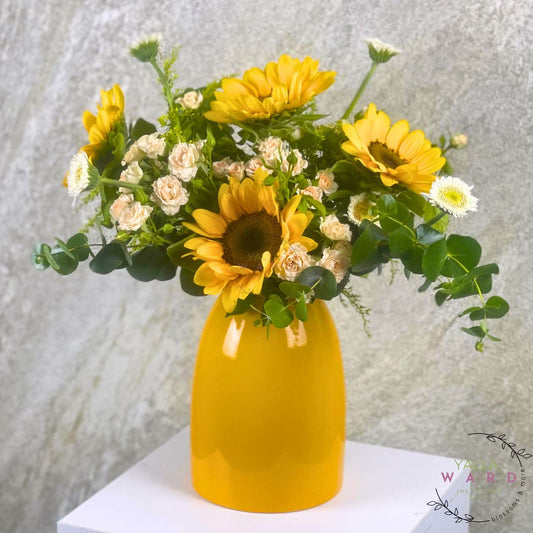 Yellow vase with sunflowers and white flowers on a textured light gray background