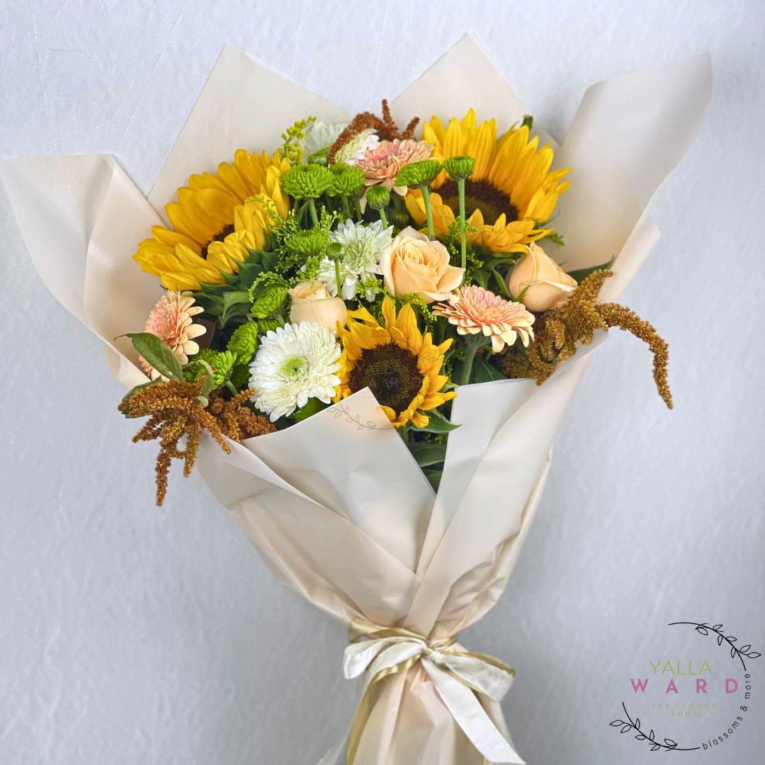 Bouquet of sunflowers and other flowers wrapped in white paper with a ribbon on a light gray background.
