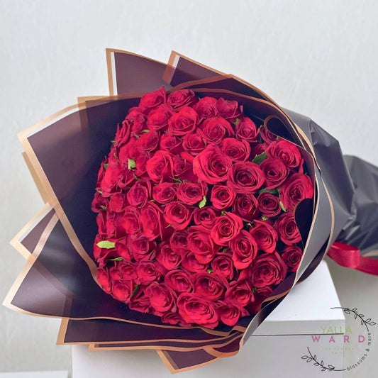 Bouquet of red roses wrapped in black paper with a gold ribbon on a light gray background.