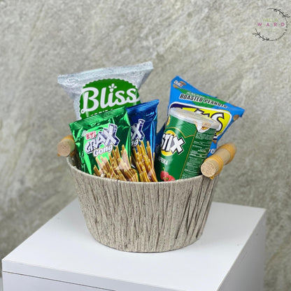 Basket with snacks including Crax, Frix, and Bliss on a white surface with a textured gray background.