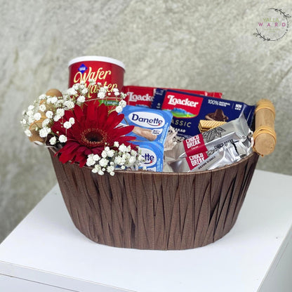 Gift basket with snacks and flowers on a white surface