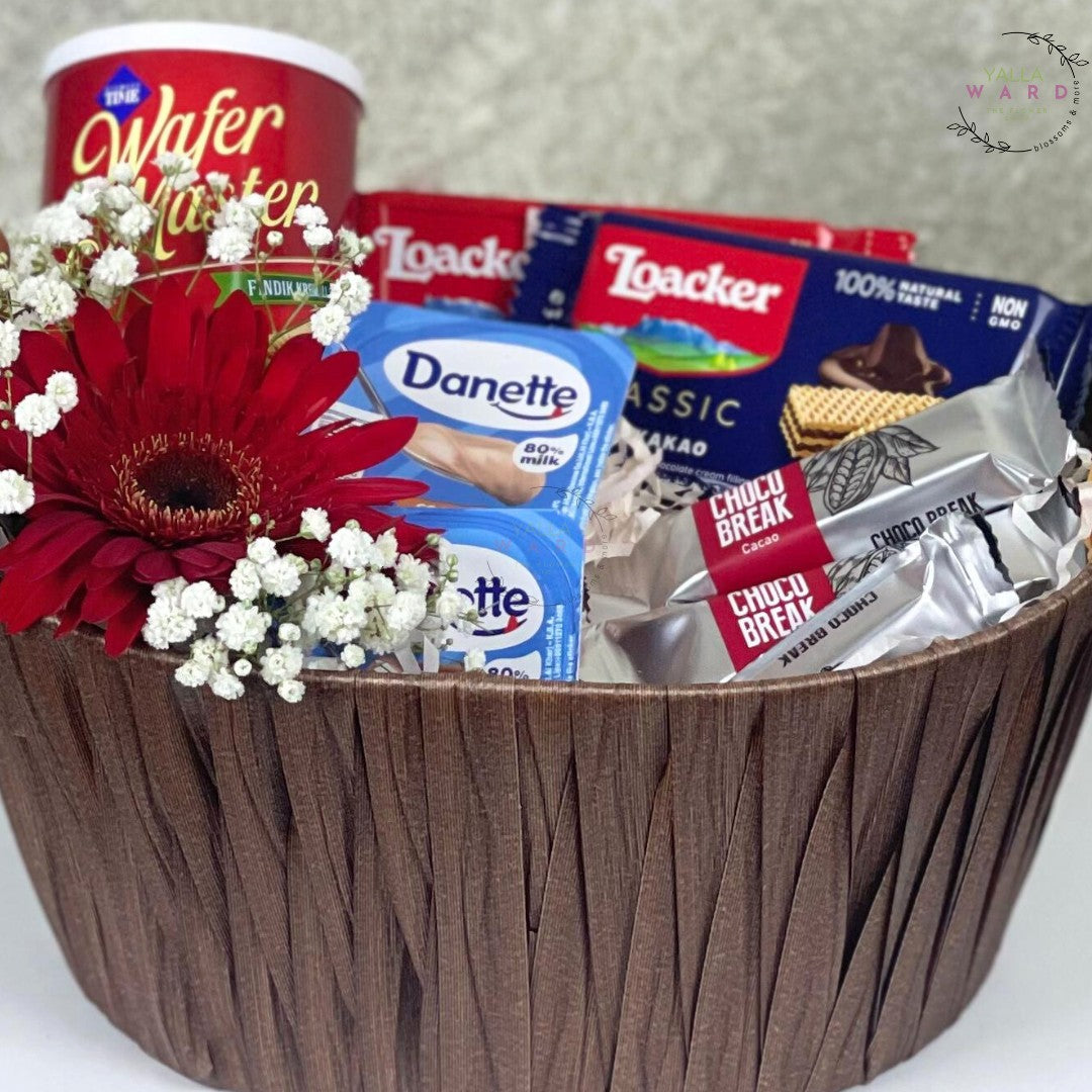 Basket with snacks, flowers, and a box of Danette on a white background