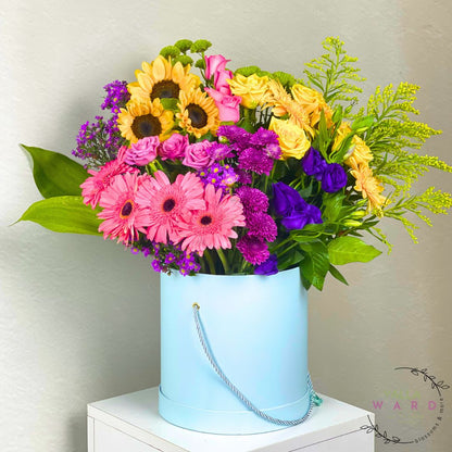 Colorful bouquet of flowers in a light blue container on a white surface with a neutral background.