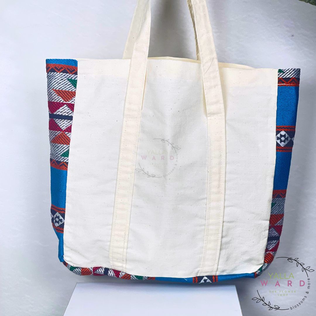 White tote bag with blue and red patterned handles on a white background