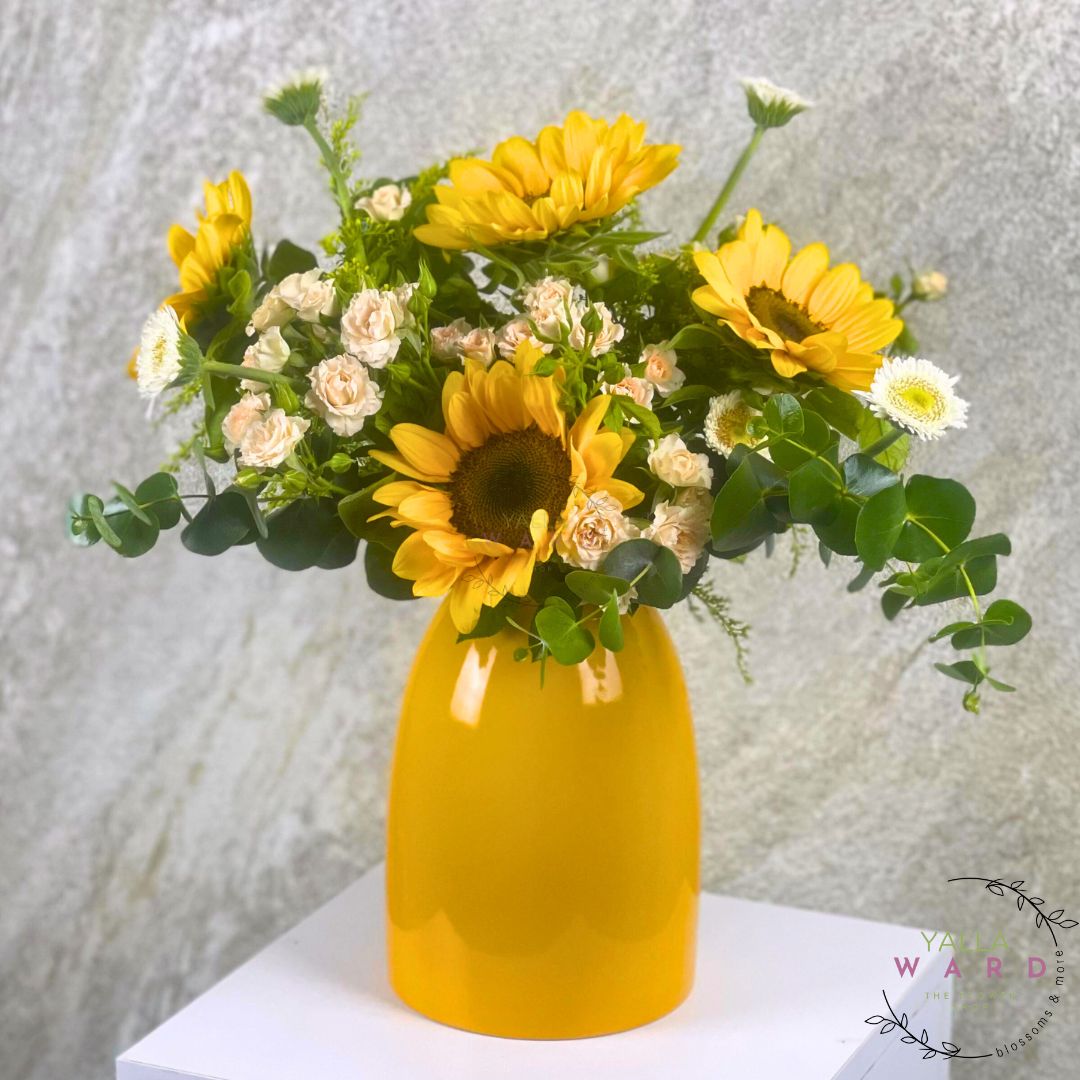 Yellow vase with sunflowers and white flowers on a textured light gray background