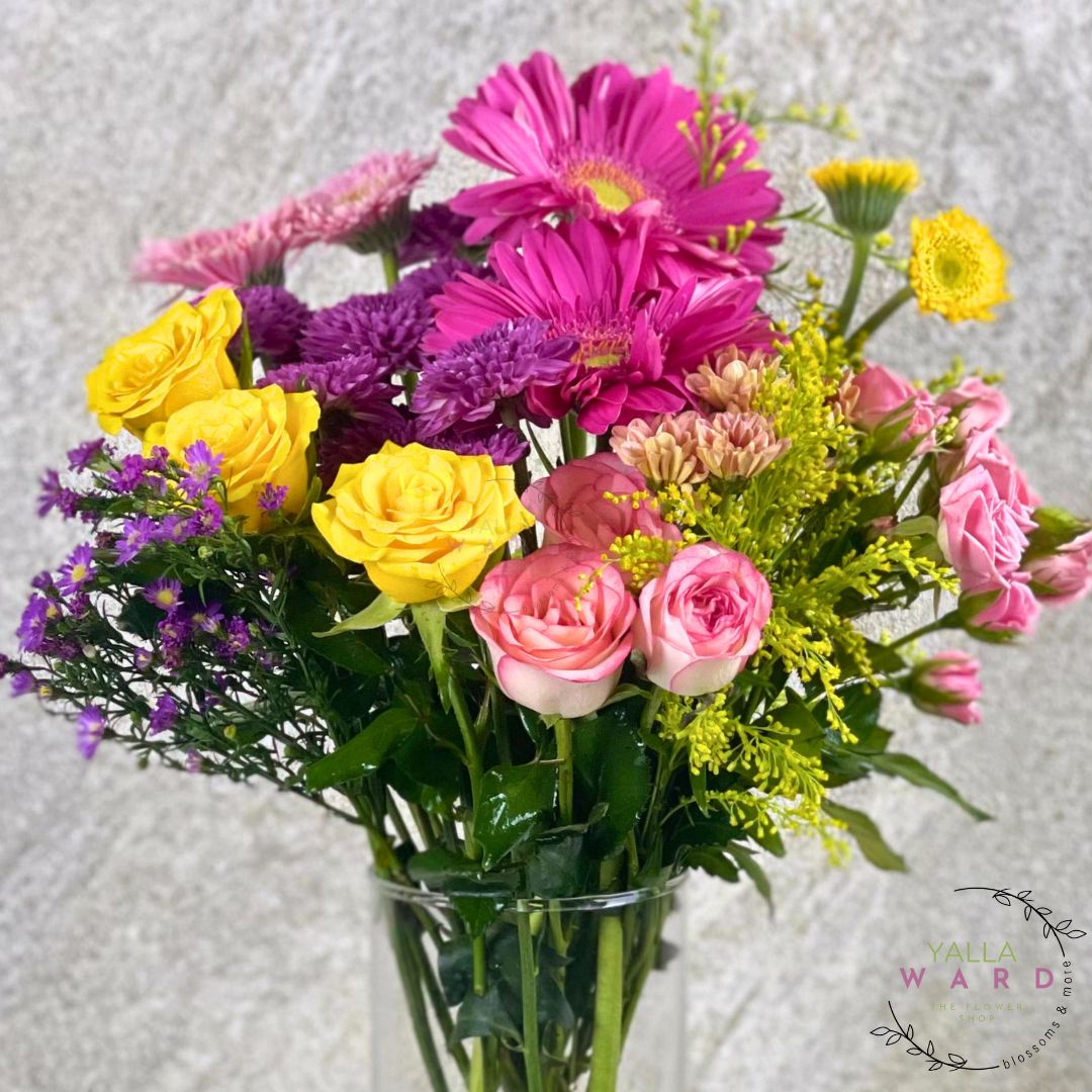 Bouquet of colorful flowers in a clear vase on a textured gray background