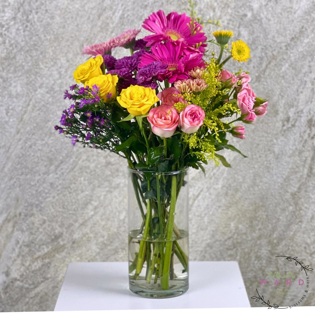 Bouquet of colorful flowers in a clear vase on a white surface with a gray textured background