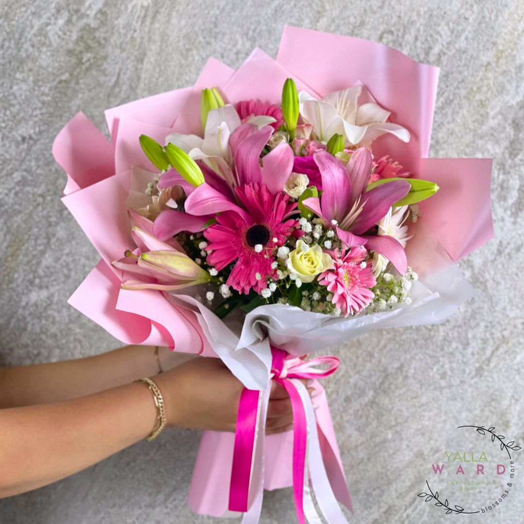 Bouquet of pink and white flowers with ribbons held by a person on a gray background