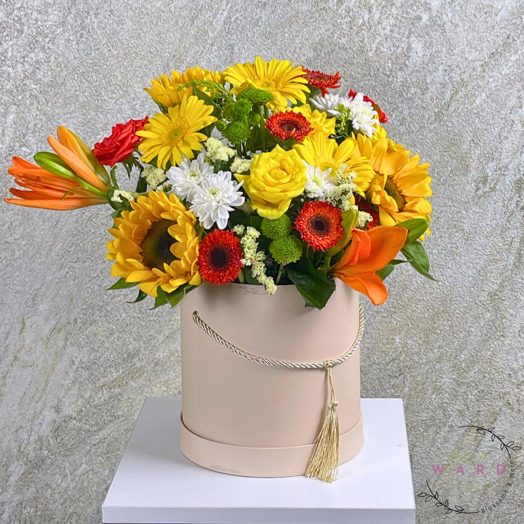 Colorful flower arrangement in a beige hatbox against a gray background