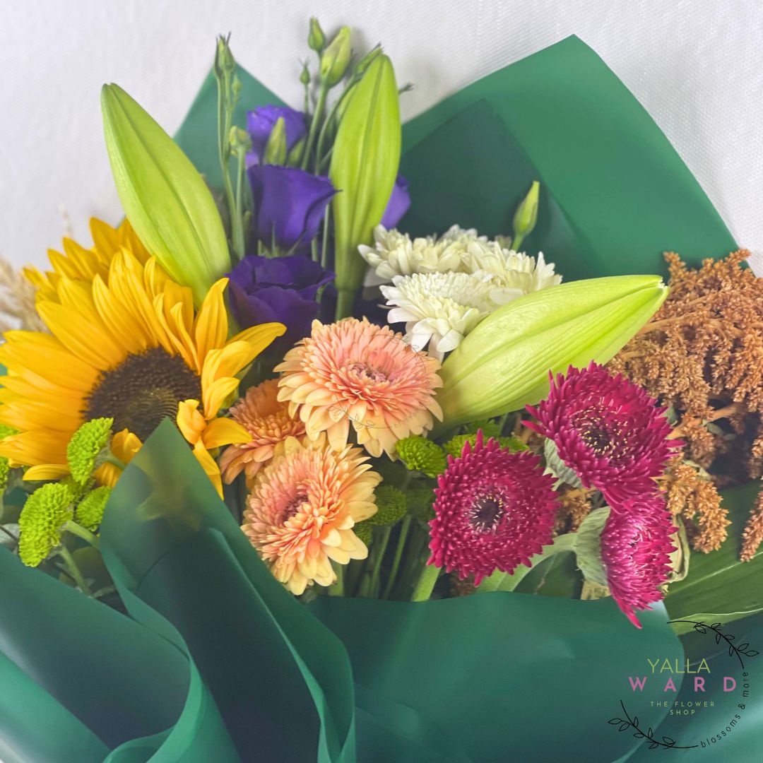Bouquet of colorful flowers wrapped in green paper with 'Yalla Ward' branding.