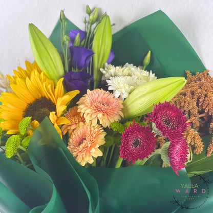 Bouquet of colorful flowers wrapped in green paper with 'Yalla Ward' branding.