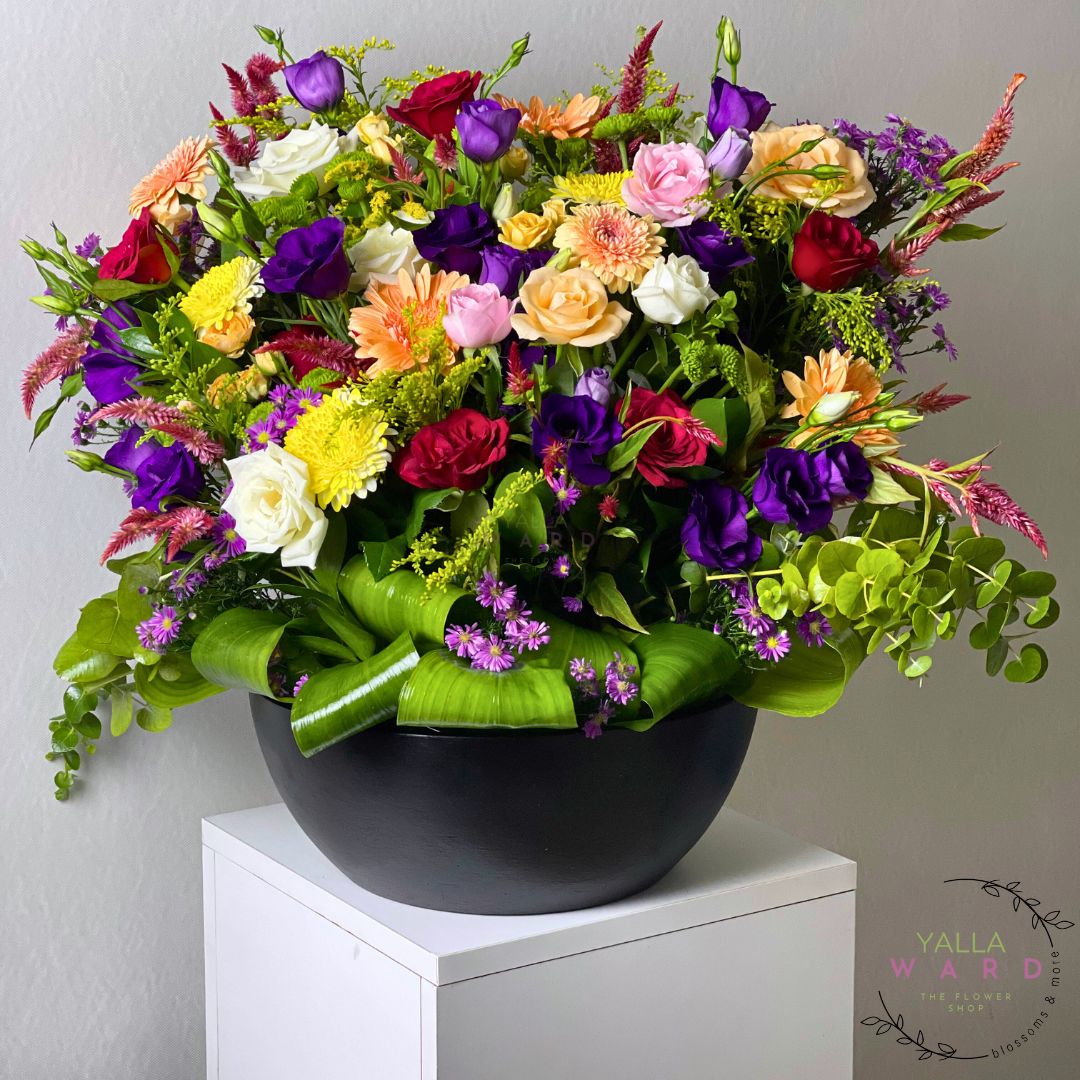 Colorful flower arrangement in a black pot on a white surface with a gray background
