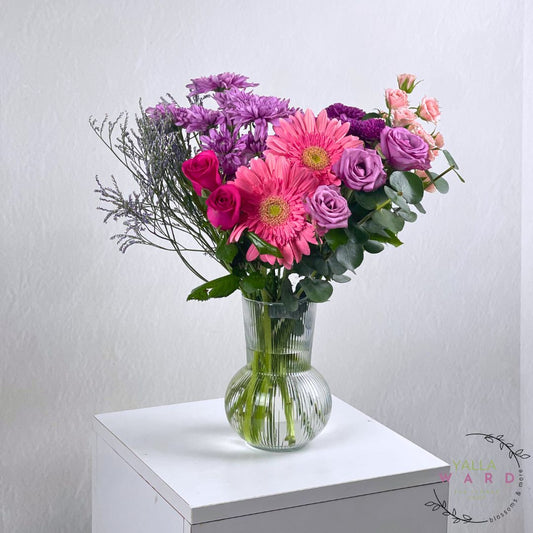 pink and purple flowers in a clear vase on a white surface with a light gray background.