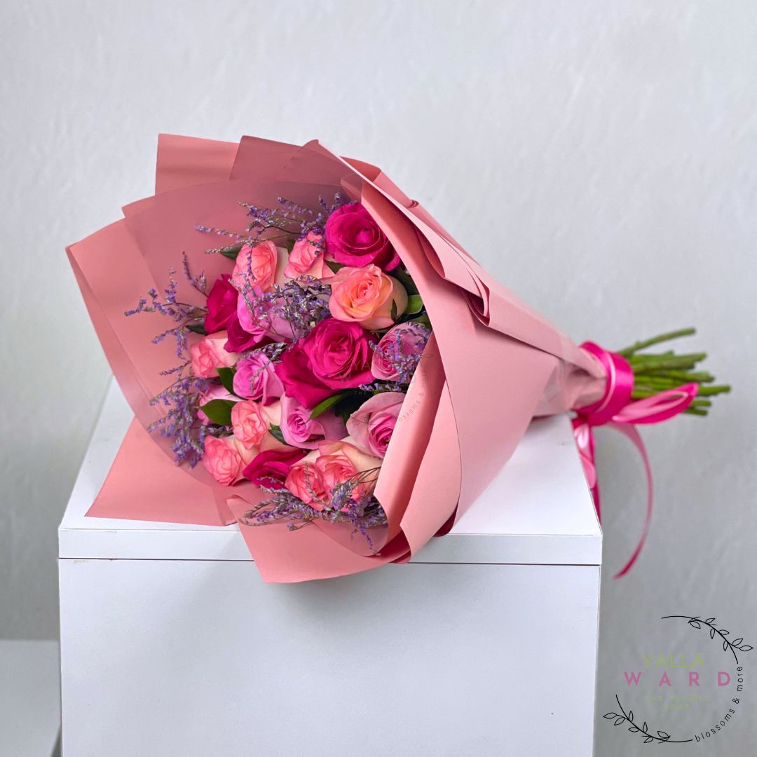 Bouquet of pink and purple roses wrapped in pink paper on a white surface with a light gray background.