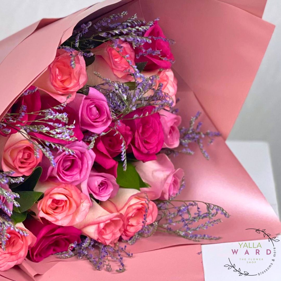 Bouquet of pink and red roses with lavender sprigs, wrapped in pink paper, on a white background.