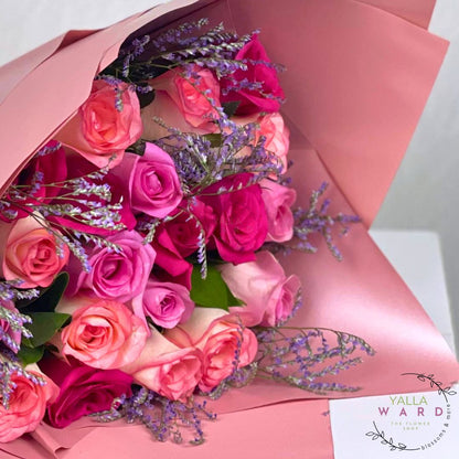 Bouquet of pink and red roses with lavender sprigs, wrapped in pink paper, on a white background.