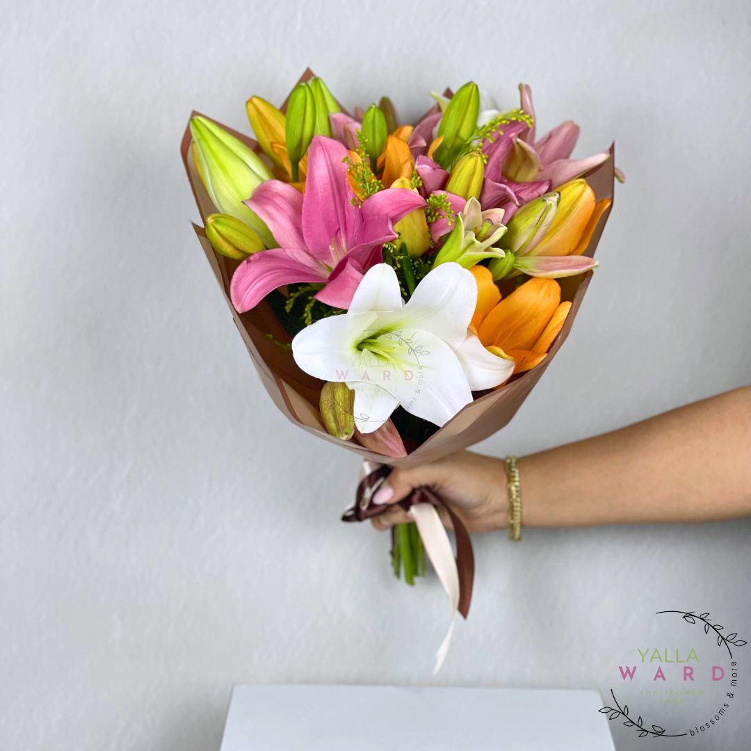 Bouquet of colorful lilies held by a hand against a light gray background, with 'Yalla Ward' branding.