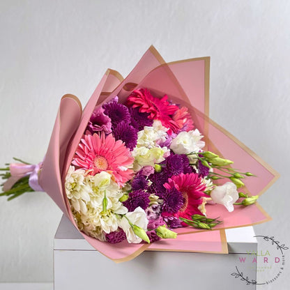 Bouquet of pink flowers wrapped in pink paper on a white surface
