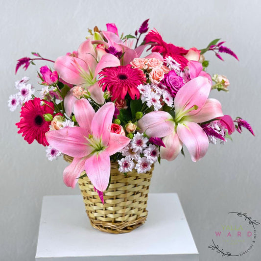pink flowers in a woven basket on a white surface with a light gray background.