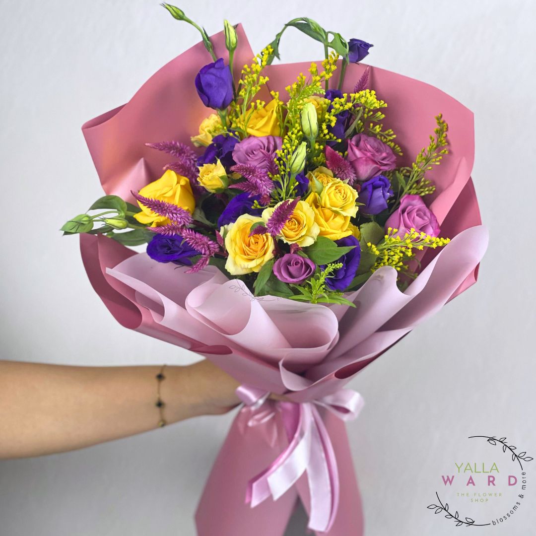 Bouquet of yellow, purple, and green flowers wrapped in pink paper with a white background.