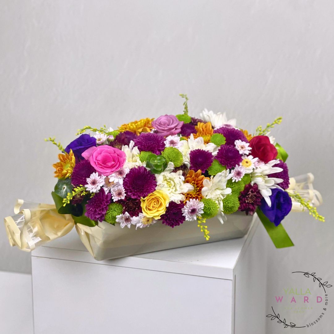 Colorful flower arrangement in a box on a white surface with a light gray background