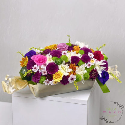 Colorful flower arrangement in a box on a white surface with a light gray background