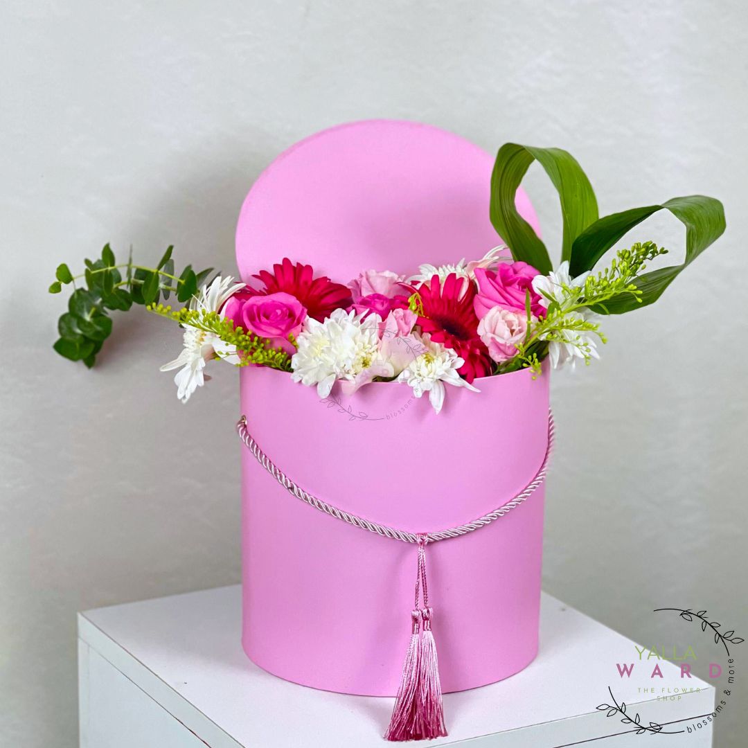 Pink flower box with colorful flowers on a white surface against a light gray background