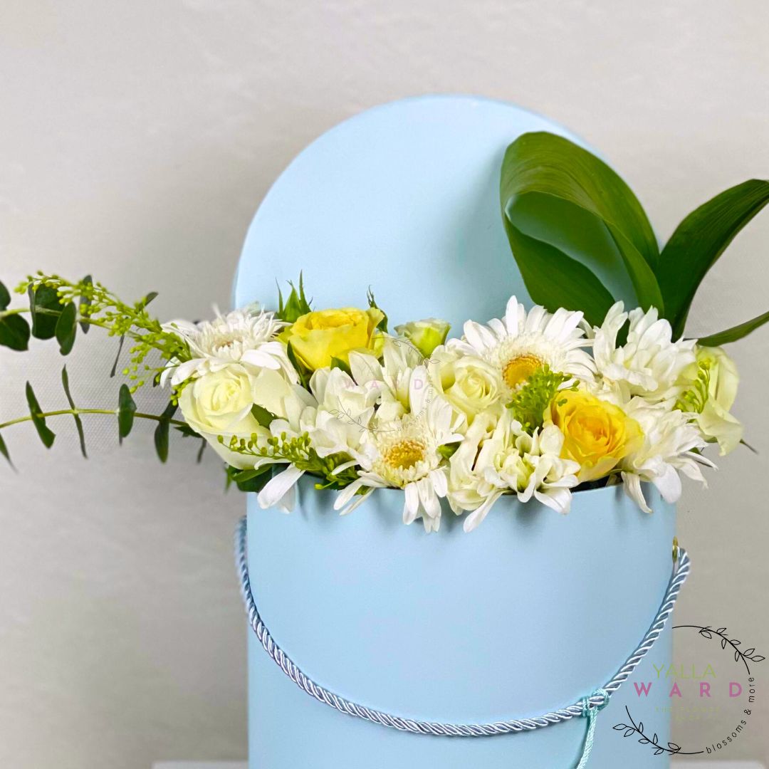Blue box on a circle with a floral arrangement of white and yellow flowers on a light gray background.