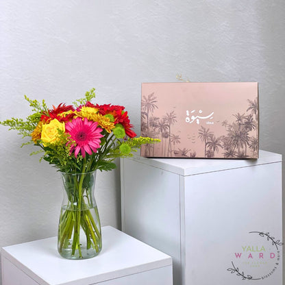 Colorful bouquet of flowers in a vase next to a dates  box on a white surface with a light gray background.
