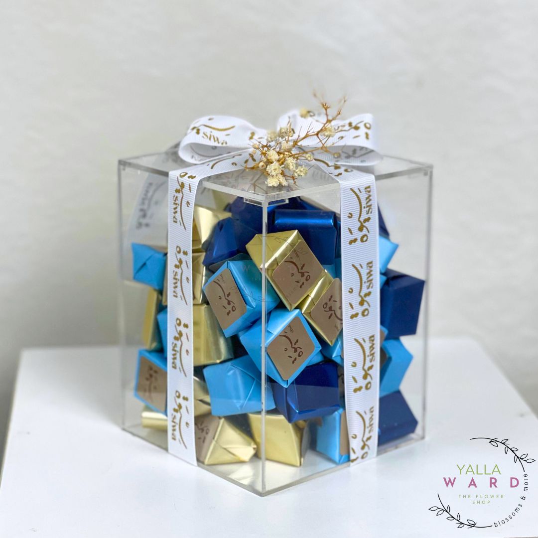 Clear gift box with blue and gold chocolate bars inside, tied with a white ribbon.