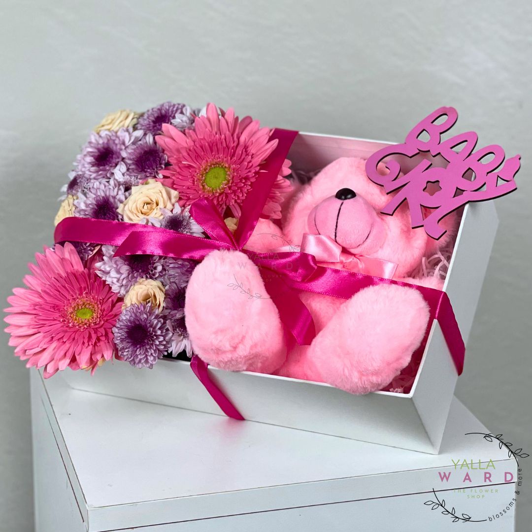 Pink teddy bear and flowers in a box with 'Love' sign on a white surface