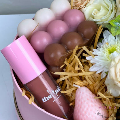 Lip gloss with pink cap and visible brand name in a decorative box with flowers