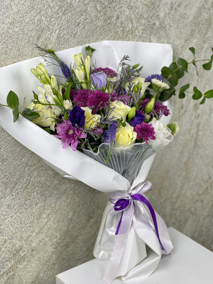 Bouquet of flowers wrapped in white paper with a purple ribbon on a neutral background