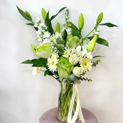 Bouquet of green and white flowers in a clear vase on a light background