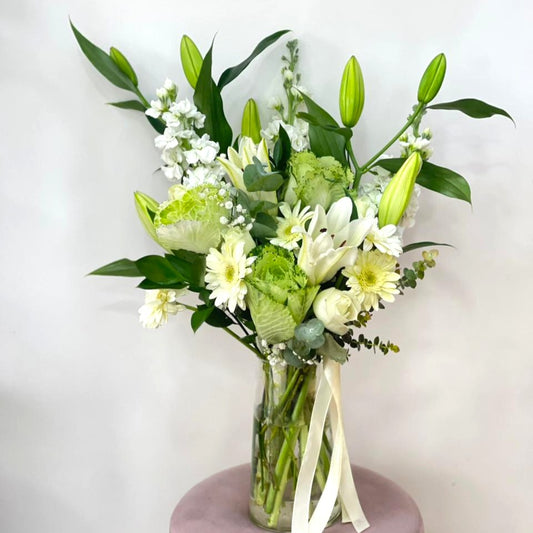 Bouquet of green and white flowers in a clear vase on a light background