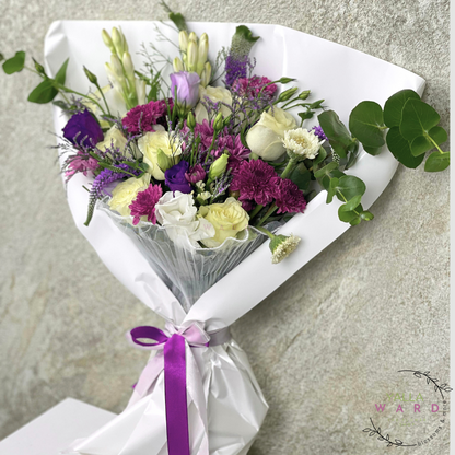 Bouquet of flowers wrapped in white paper with a purple ribbon on a gray surface.