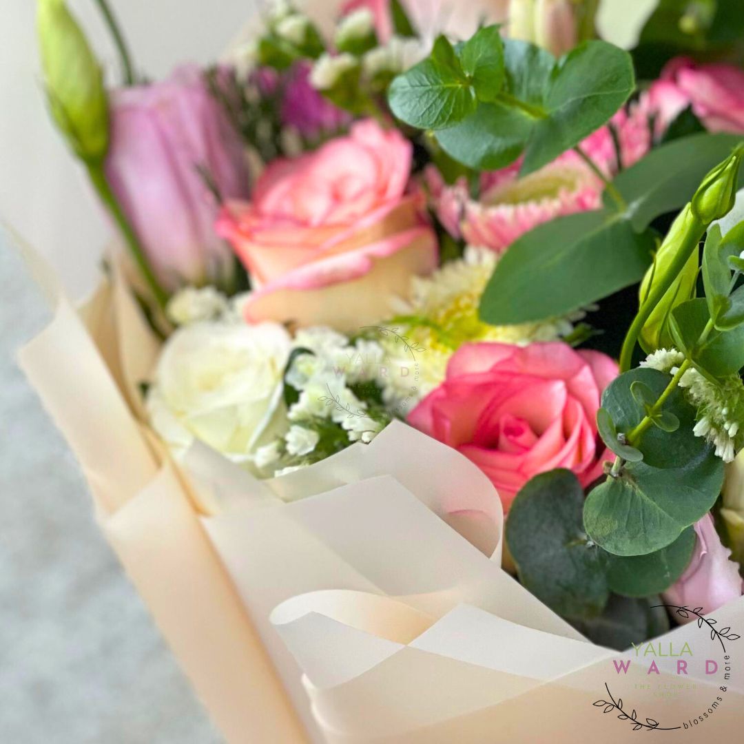Bouquet of pink and green flowers wrapped in white paper with 'yalla Ward' branding.