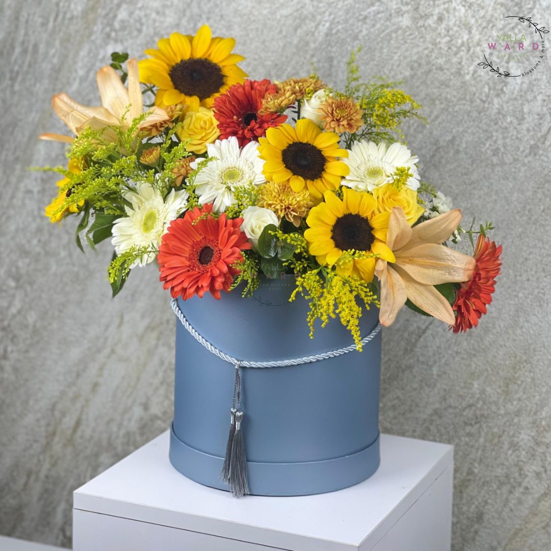 Colorful flower arrangement in a blue hat box against a gray background
